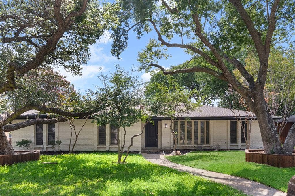 1612 Northcrest Drive, Plano, TX 75075 White brick exterior with a dark roofline, mature trees, a manicured lawn, and a curved walkway