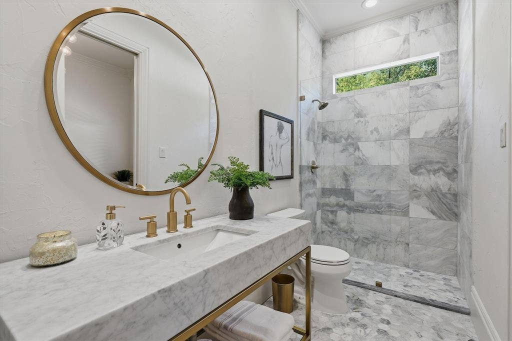 First floor guest ensuite bath is beautifully remodeled featuring marble finishes, a glass-enclosed shower and refined brass fixtures.