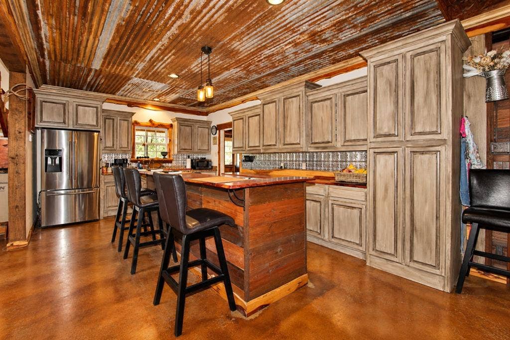 7245 County Road 4095, Kaufman, TX 75142 Kitchen featuring a corrugated metal ceiling, wood-finish flooring, custom cabinetry with a distressed finish, a center island with a wood base, and a tiled backsplash