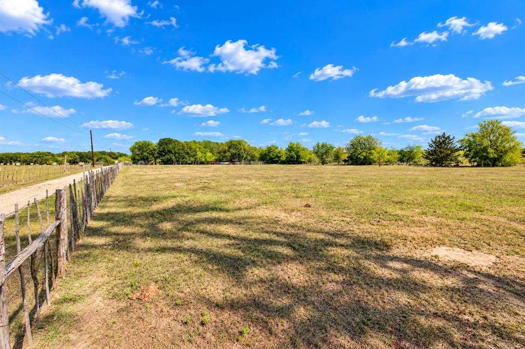 7245 County Road 4095, Kaufman, TX 75142 Expansive open field with scattered trees and a natural wood-post fence bordering a gravel path