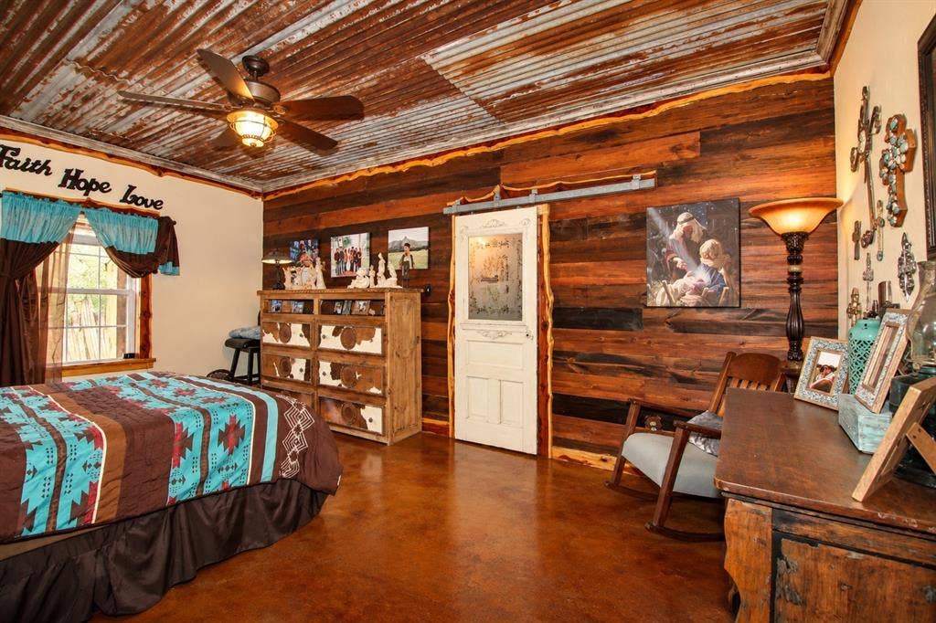 7245 County Road 4095, Kaufman, TX 75142 Corrugated metal ceiling with a ceiling fan, wood plank wall paneling, stained concrete flooring, and a sliding barn door