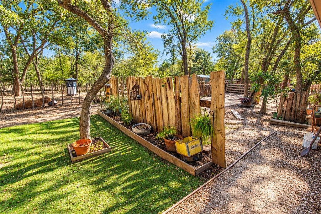 7245 County Road 4095, Kaufman, TX 75142 Expansive outdoor space featuring mature trees, a manicured lawn, a gravel pathway, a custom wood privacy fence, and a raised planter bed
