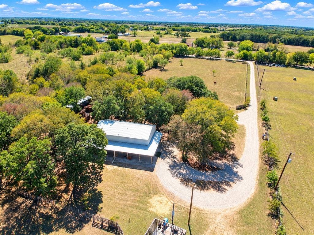 7245 County Road 4095, Kaufman, TX 75142 Expansive property featuring a gravel driveway, mature trees, open land, and a single-story structure with a covered porch