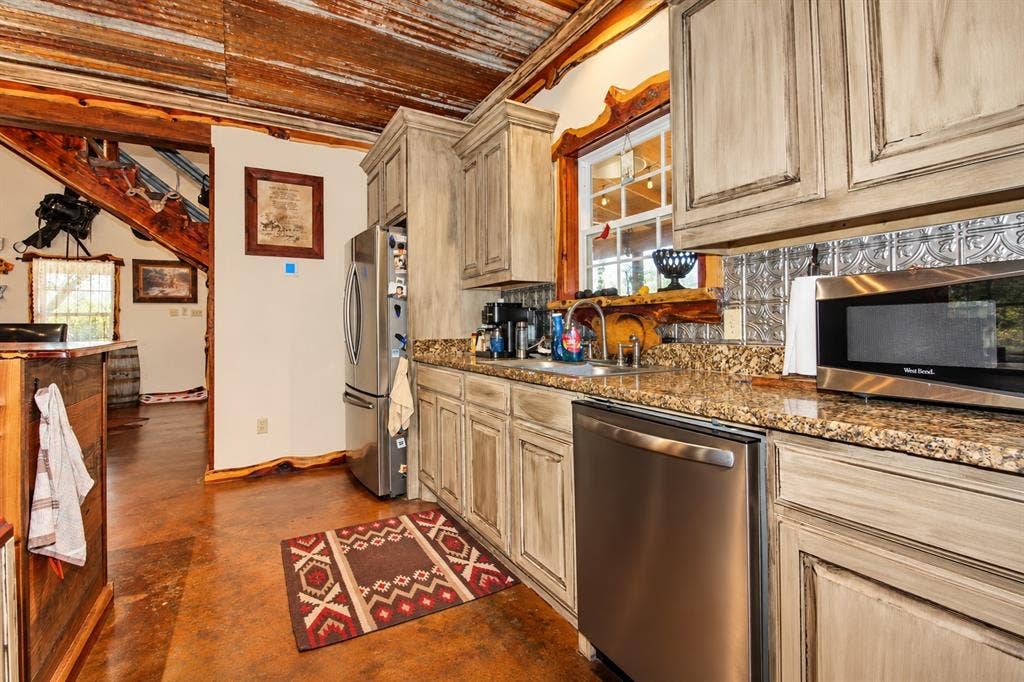 7245 County Road 4095, Kaufman, TX 75142 Kitchen featuring distressed cabinetry, granite countertops, stainless steel appliances, a decorative metal backsplash, and a corrugated metal ceiling