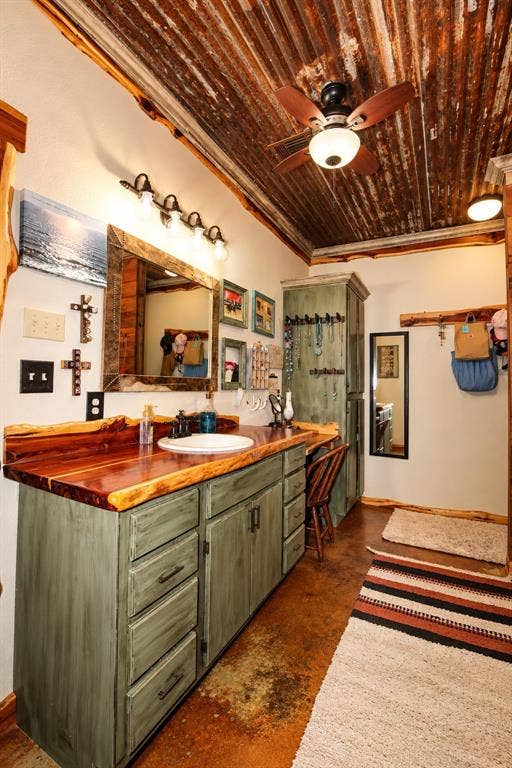 7245 County Road 4095, Kaufman, TX 75142 Vaulted ceiling with corrugated metal, wood-finish vanity with an integrated sink, natural wood countertop, decorative wall mirror, and ceiling fan with lighting