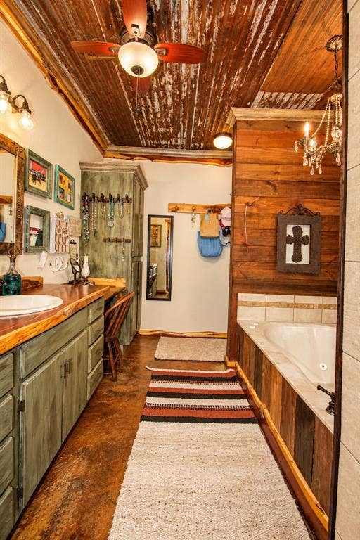 7245 County Road 4095, Kaufman, TX 75142 Distressed metal ceiling with a ceiling fan, dual vanity with a wood countertop, built-in soaking tub, and wood paneling