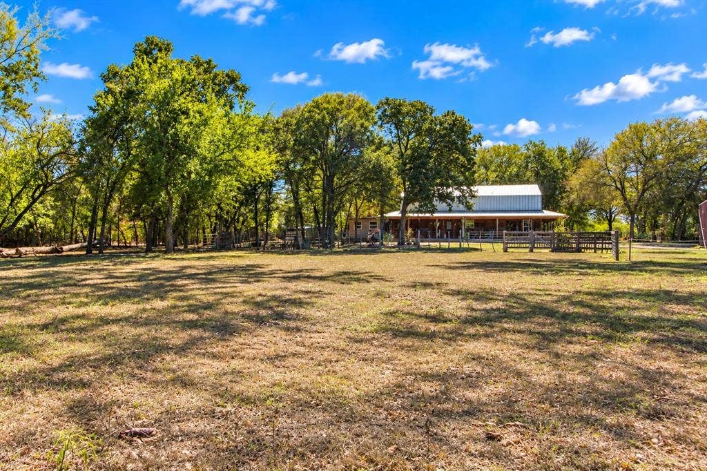 7245 County Road 4095, Kaufman, TX 75142 Expansive open field with scattered mature trees and a distant structure featuring a covered porch and metal roof