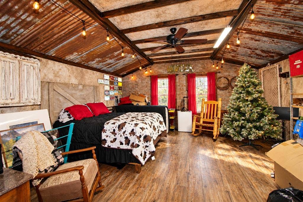7245 County Road 4095, Kaufman, TX 75142 Vaulted ceiling with exposed wood beams and corrugated metal panels, wood-finish flooring, two windows with red drapes, and a ceiling fan with integrated lighting