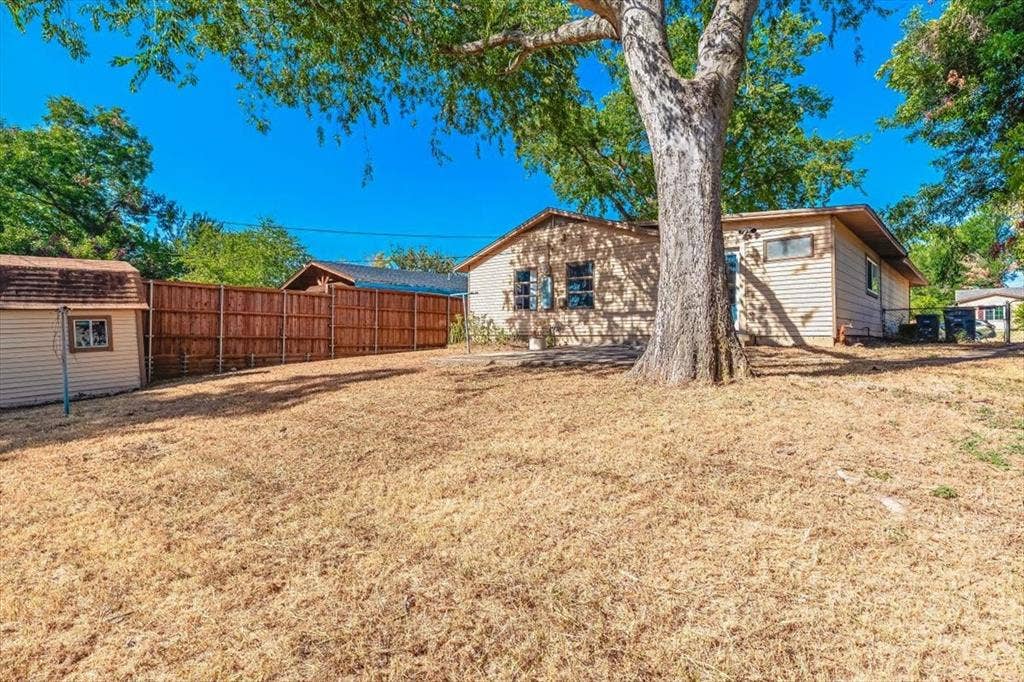 12326 Dandridge Drive, Dallas, TX 75243 Expansive backyard featuring a large tree, wood privacy fence, and an auxiliary storage shed