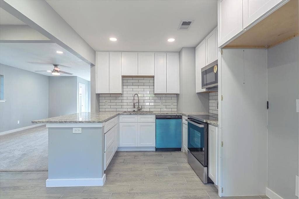 12326 Dandridge Drive, Dallas, TX 75243 U-shaped kitchen featuring white cabinetry, light-toned countertops, a subway tile backsplash, stainless steel appliances, and wood-finish flooring