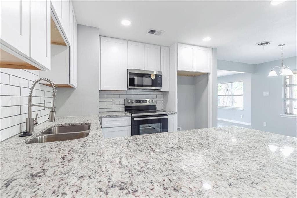 12326 Dandridge Drive, Dallas, TX 75243 Kitchen featuring light-toned granite countertops, white cabinetry, a stainless steel sink with a gooseneck faucet, a subway tile backsplash, and stainless steel appliances