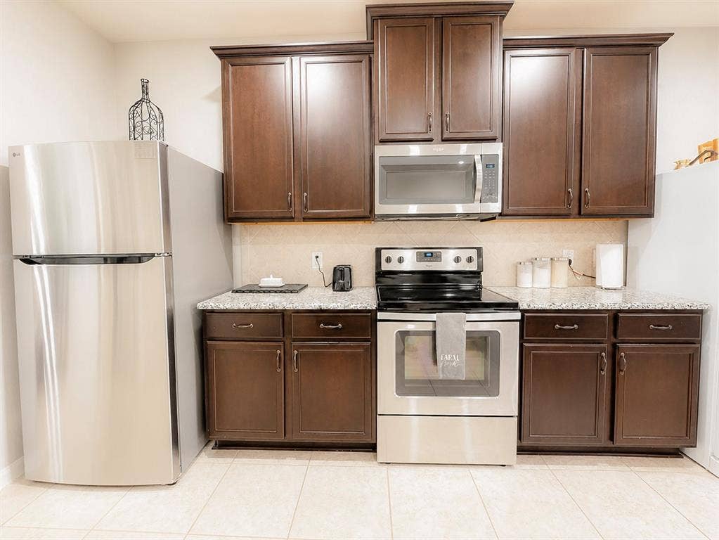 Kitchen featuring wood-finish cabinetry, granite-style countertops, stainless steel appliances, and a tiled floor