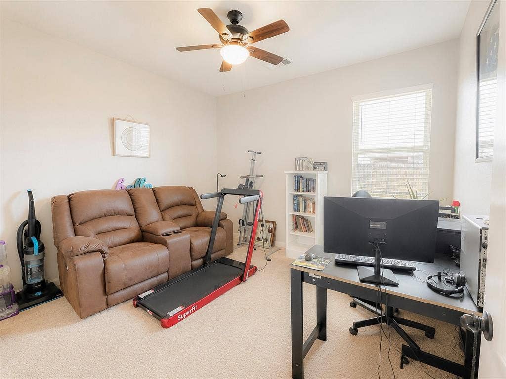 Neutral wall color, light-colored carpeting, window with blinds, ceiling fan with integrated lighting, and a built-in bookshelf
