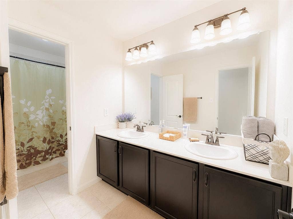 Dual sink vanity with dark wood-finish cabinetry, light-toned countertop, and full-width mirror