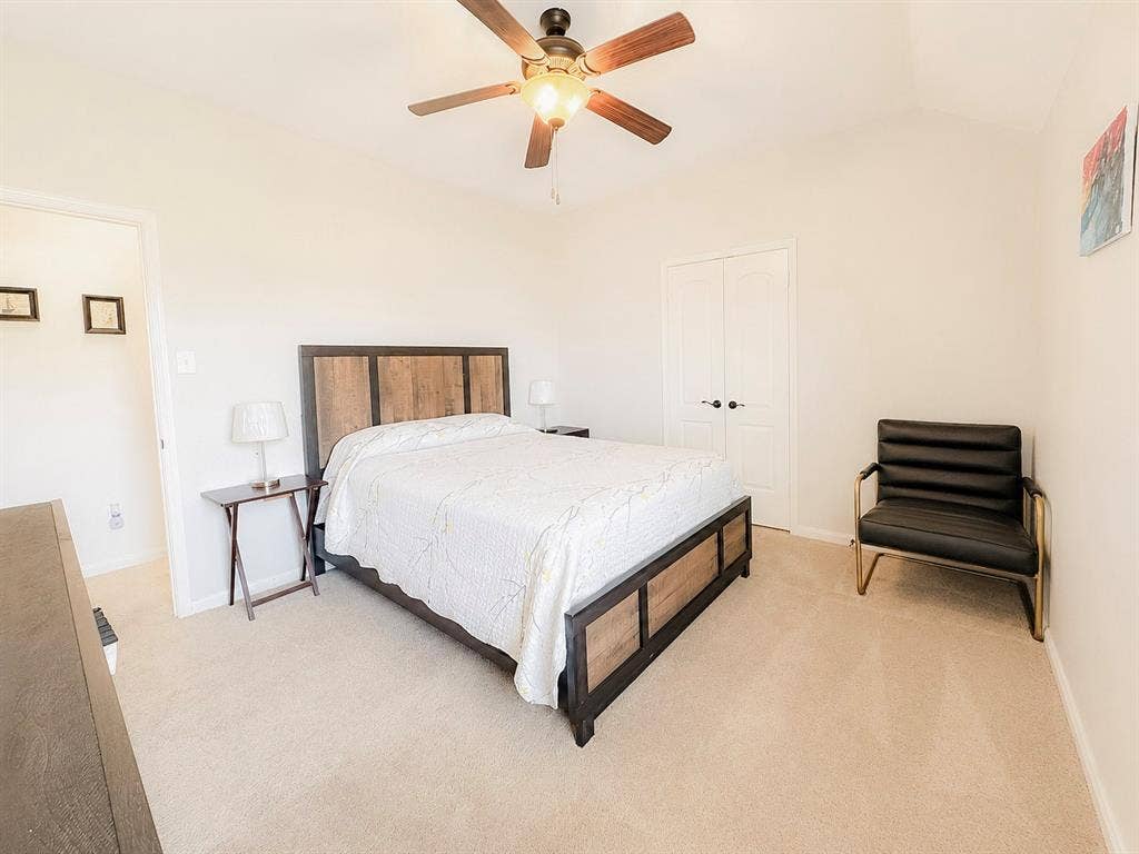 Neutral tone carpeting, vaulted ceiling, and a ceiling fan with light fixture