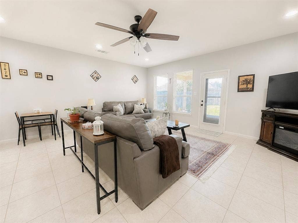 Recessed lighting throughout, ceiling fan with wood-finish blades, light-toned tile flooring, multiple windows, and a glass-paneled door