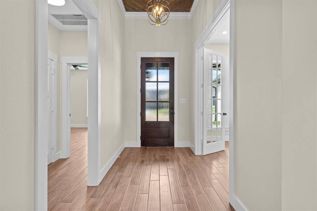 Wood-finish flooring, dark wood entry door with frosted glass, coffered ceiling with wood paneling, decorative ceiling light fixture, and white French doors