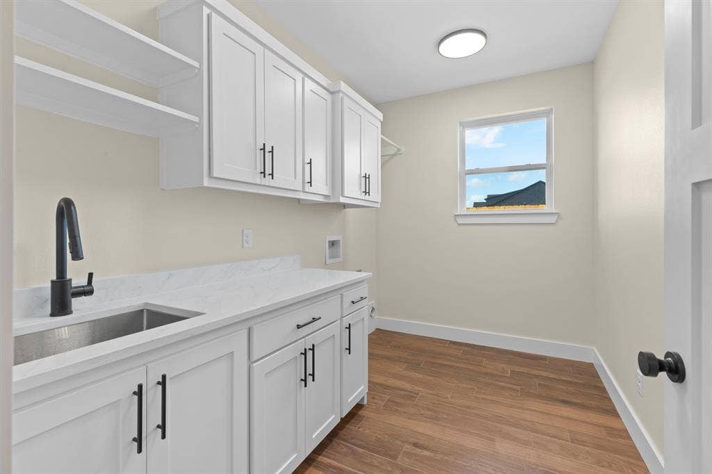 White cabinetry with matte black hardware, integrated stainless steel sink, expansive white countertop, wood-finish flooring, and a single window