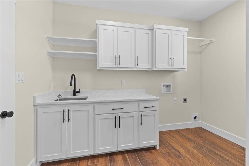 White shaker cabinetry, stone-finish countertop, undermount sink with a matte black faucet, and wood-finish flooring