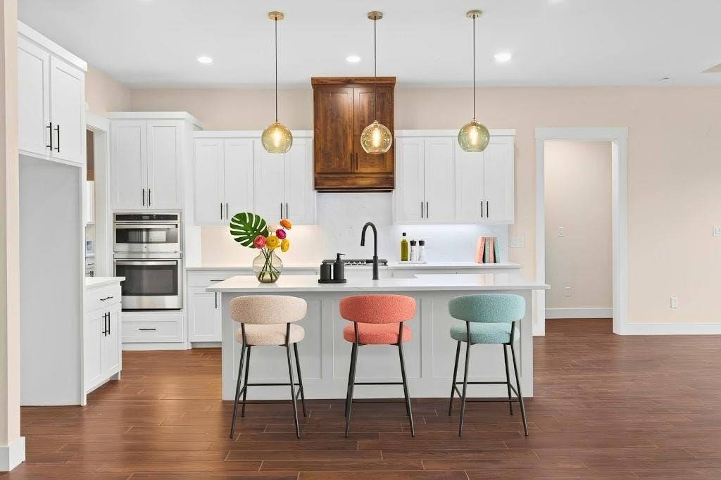 Kitchen featuring white cabinetry, built-in stainless steel appliances, a center island with sink, three pendant lights, and wood-finish flooring