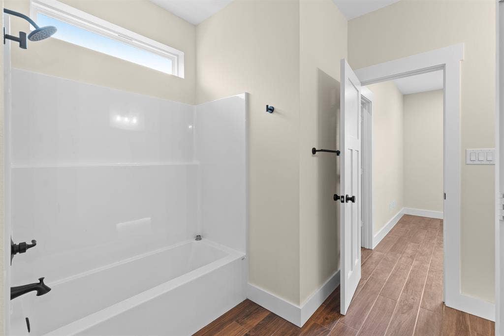 White bathtub with a shower, transom window, dark bronze showerhead, dark bronze faucet, and wood-finish flooring