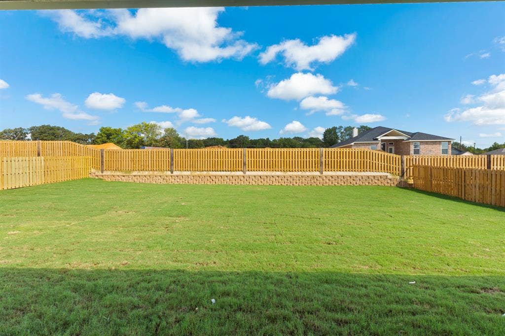 Expansive backyard featuring a lush lawn, wood privacy fencing, and a retaining wall