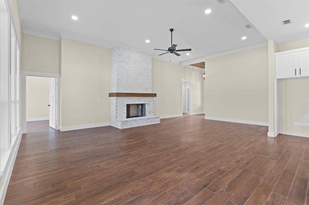 Expansive room with wood-finish flooring, a white brick fireplace with a wood mantle, and recessed lighting