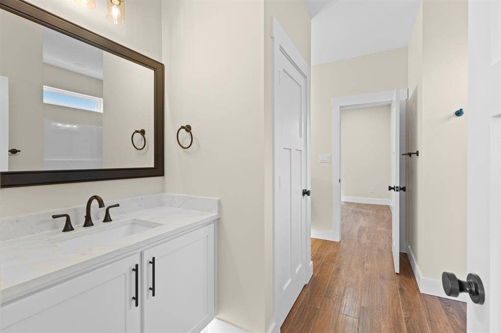 White vanity with integrated sink, black hardware, framed mirror, and wood-finish flooring