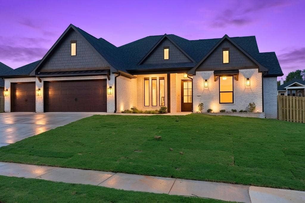 Brick exterior with dark shake siding accents, multiple gables, a three-car garage, and a wood privacy fence