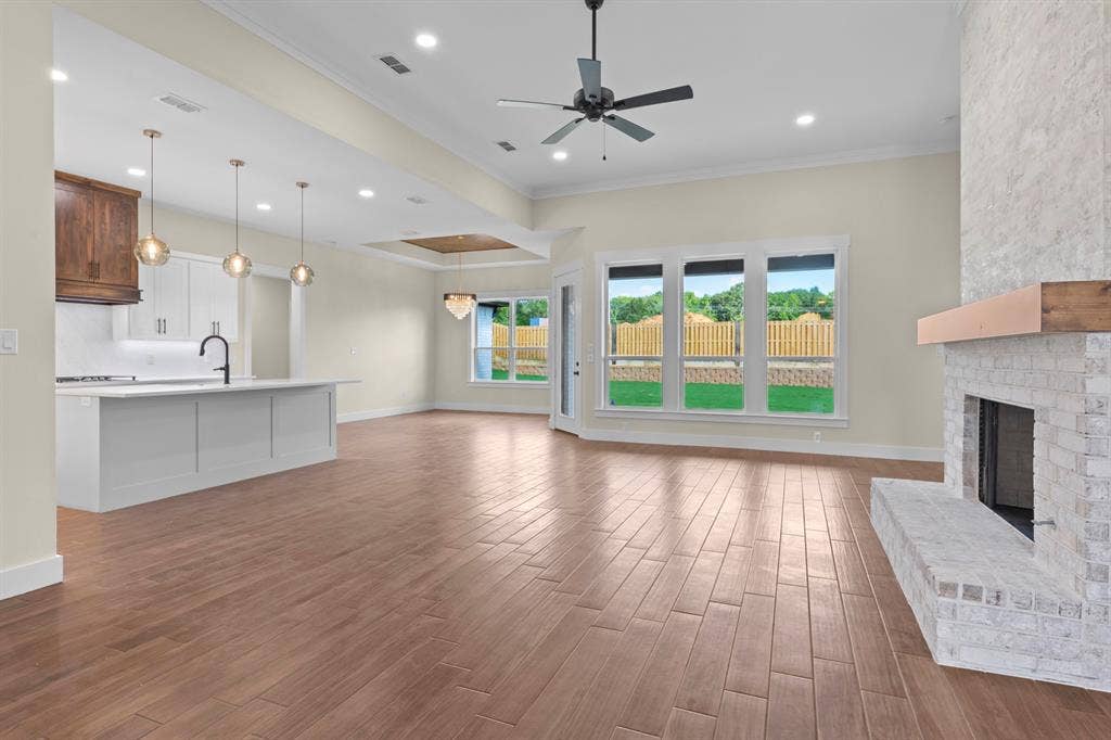 Open-concept living space featuring wood-finish flooring, a white brick fireplace with a wood mantel, and an island kitchen with pendant lighting