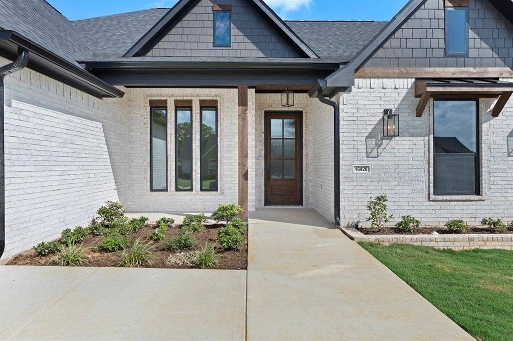 White brick exterior with dark trim, shake siding accent, black-framed windows, and a wood-paneled front door