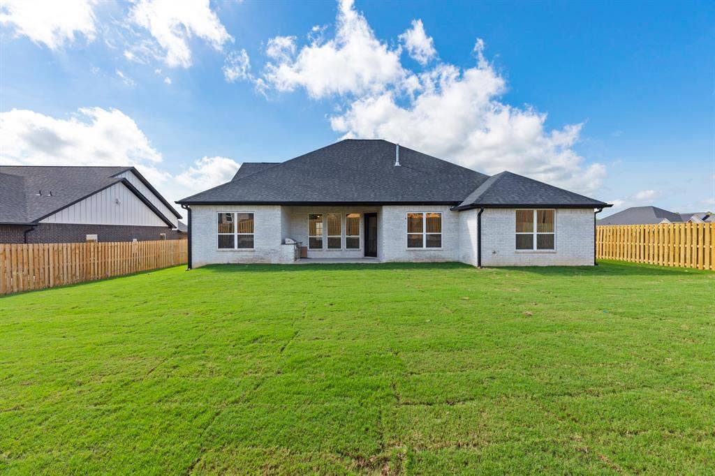 Expansive backyard featuring a manicured lawn, full privacy fencing, and a white brick exterior