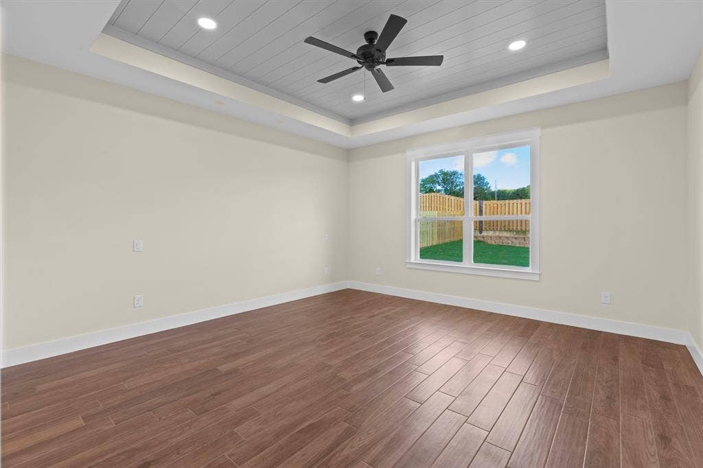 Tray ceiling with recessed lighting and a ceiling fan, wood-finish flooring, and a large window