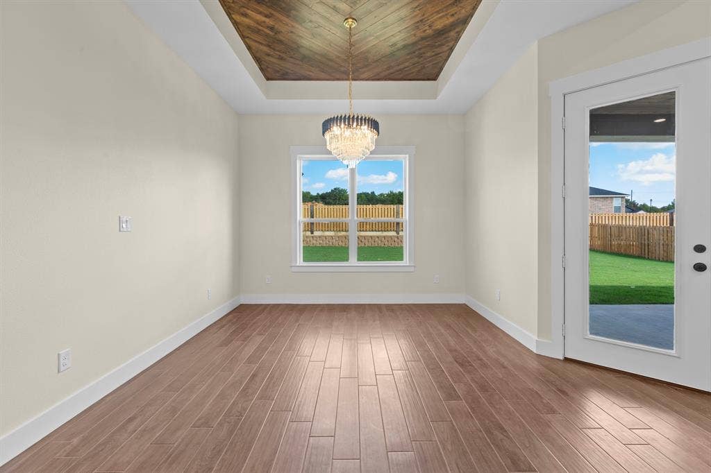 Tray ceiling with wood-finish inlay, large window, wood-finish flooring, and glass-paneled door