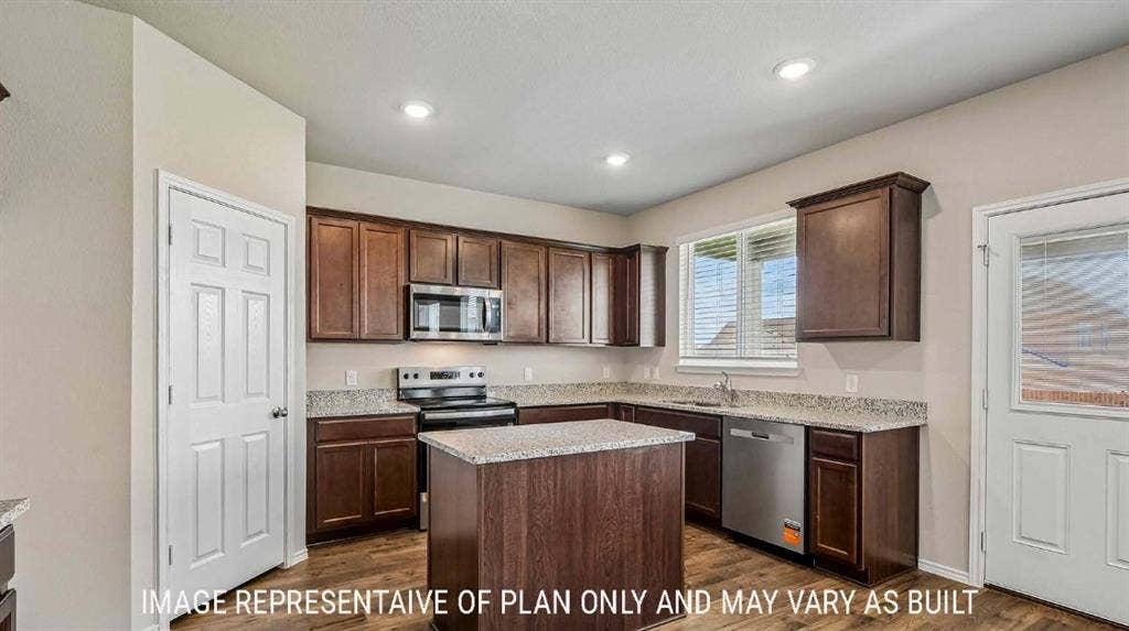 Kitchen featuring wood-finish cabinetry, granite-style countertops, stainless steel appliances, a center island, and wood-finish flooring