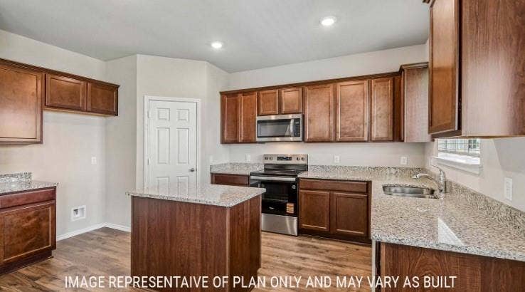 Kitchen featuring wood-finish cabinetry, speckled countertops, stainless steel appliances, a kitchen island, and recessed lighting