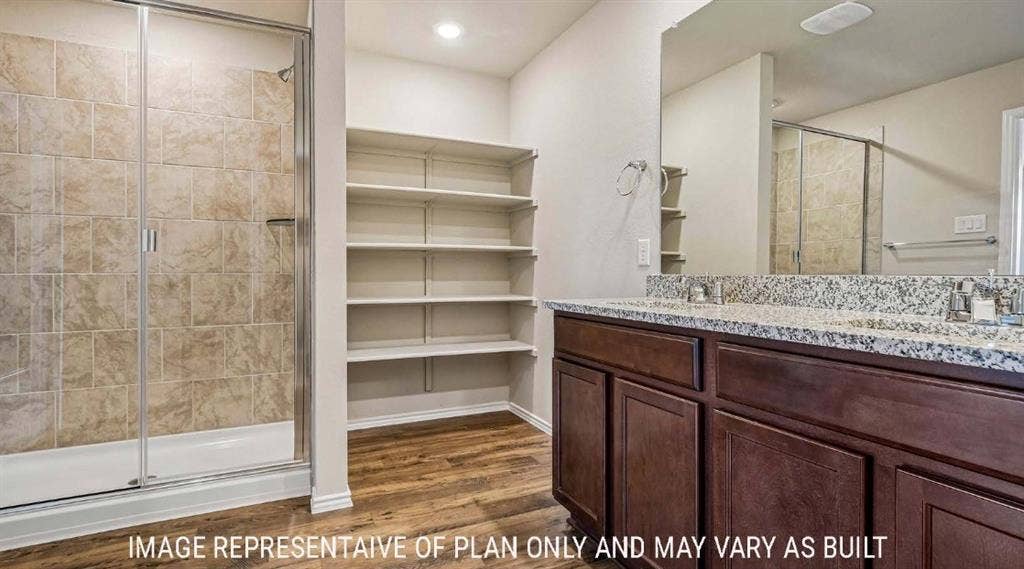Wood-finish flooring, shower with glass enclosure, wall-mounted shelving, dual vanity with undermount sinks, and speckled countertop