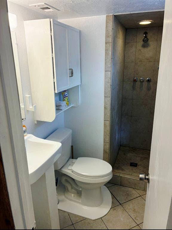 3009 Plumtree Lane, Plano, TX 75074 Pedestal sink, wall-mounted storage cabinetry, built-in shower with tile surround, and tiled flooring