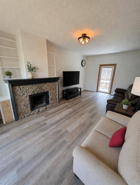 3009 Plumtree Lane, Plano, TX 75074 Stone fireplace with a dark wood mantel, wood-finish flooring, built-in shelving, and a glass-paned door