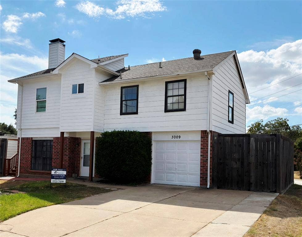 3009 Plumtree Lane, Plano, TX 75074 White siding exterior with brick accents, black-framed windows, an attached garage, a privacy fence, and a concrete driveway