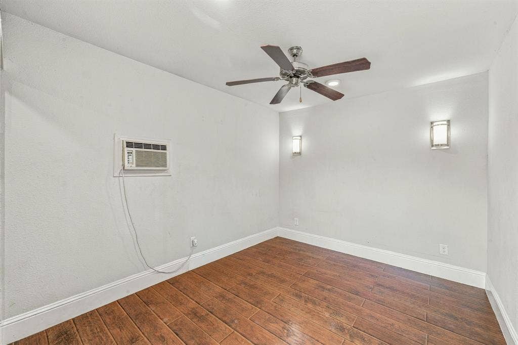 13706 Janwood Lane, Farmers Branch, TX 75234 Room featuring wood-finish tile flooring, ceiling fan with light kit, two wall-mounted sconces, and a wall-installed air conditioning unit