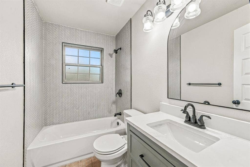 13706 Janwood Lane, Farmers Branch, TX 75234 Bathroom featuring a herringbone-patterned tile shower surround, vanity with a solid surface countertop, arched mirror, matte black plumbing fixtures, and glass-globe wall-mounted lighting