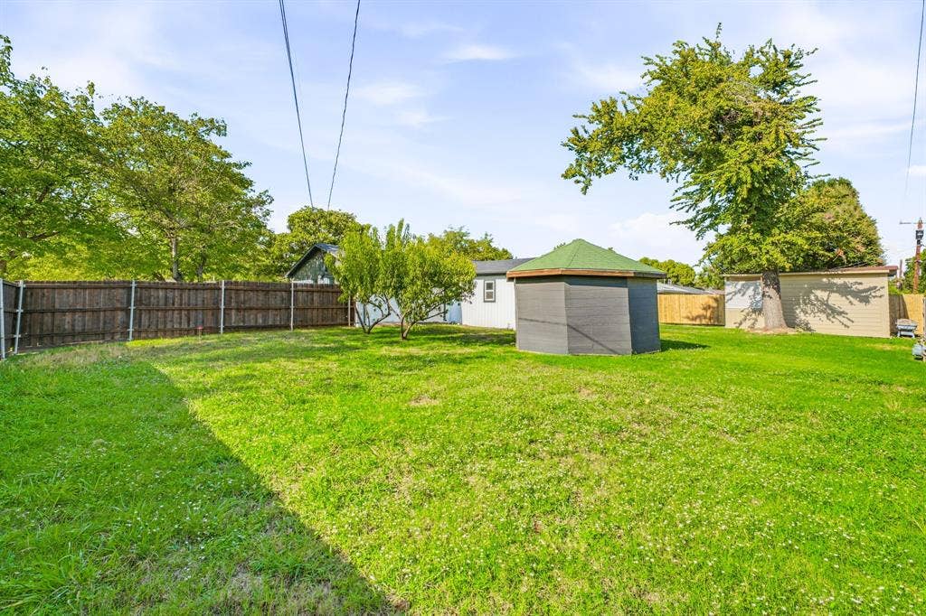 13706 Janwood Lane, Farmers Branch, TX 75234 Expansive backyard featuring a wood fence, mature trees, a detached storage structure, and a hexagonal pavilion
