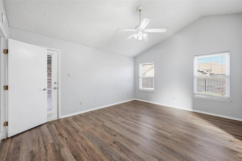 6421 Fairview Drive, Watauga, TX 76148 Vaulted ceiling with a ceiling fan, wood-finish flooring, two windows with blinds, and a door with an integrated blind