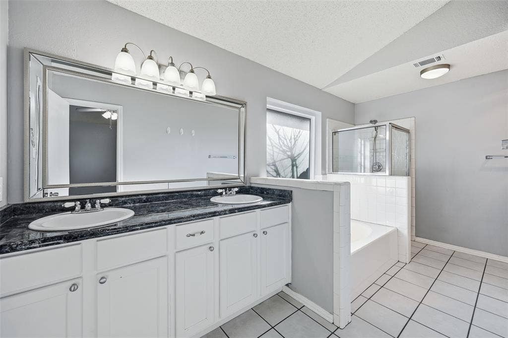 6421 Fairview Drive, Watauga, TX 76148 Dual vanity with undermount sinks, stone-finish countertop, white cabinetry, a framed mirror, and a built-in shower and tub combination