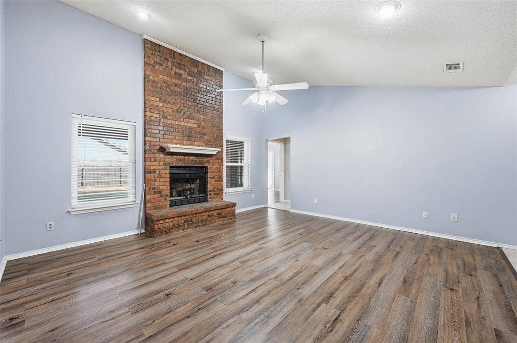 6421 Fairview Drive, Watauga, TX 76148 Spacious room featuring vaulted ceilings, wood-finish flooring, a brick fireplace with a mantel, and dual windows