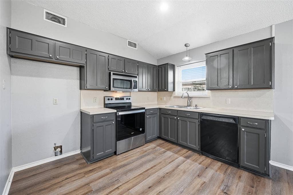6421 Fairview Drive, Watauga, TX 76148 Kitchen featuring abundant gray cabinetry, light-toned countertops, wood-finish flooring, stainless steel microwave, and a stainless steel range