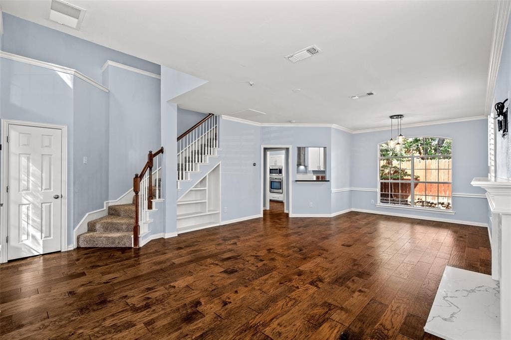 14592 Aspen Court, Addison, TX 75001 Hardwood-finish flooring throughout, white crown molding, built-in shelving under staircase, fireplace with a white mantel and light-toned hearth, and a window with garden scenery