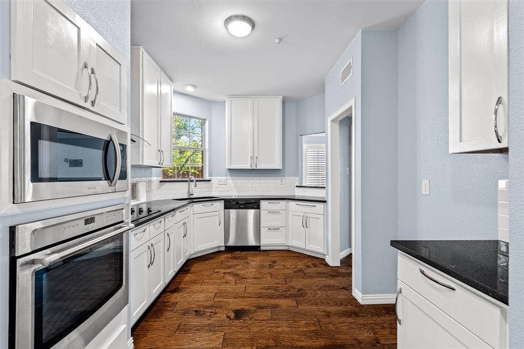 14592 Aspen Court, Addison, TX 75001 Kitchen featuring white cabinetry, dark countertops, built-in stainless steel appliances, wood-finish flooring, and a white subway tile backsplash