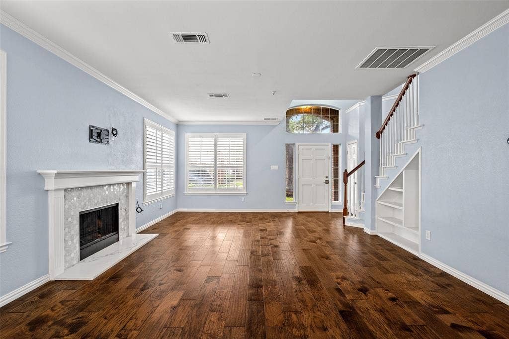 14592 Aspen Court, Addison, TX 75001 Wood-finish flooring, white fireplace mantel with tile surround, white plantation shutters, staircase with dark wood handrail, and built-in shelving under stairs